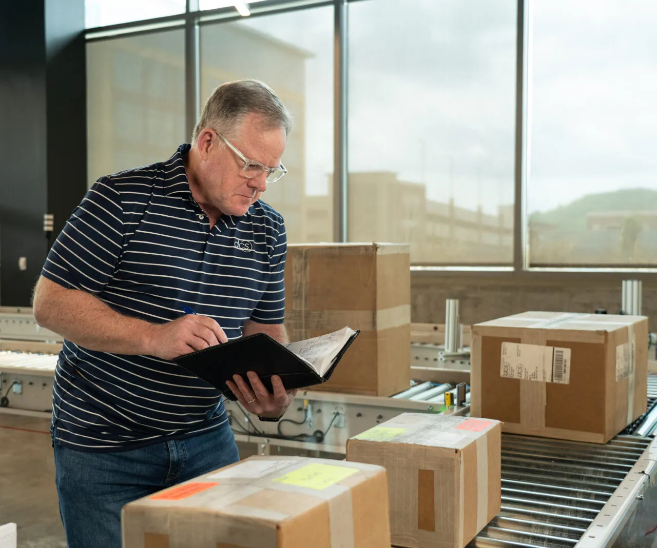 Asure Page Image Man checking notebook and packages on a DCS conveyor